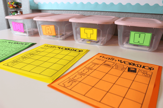 Four math bins with the letters MATH printed on them and colorful math workshop papers in front of them. 