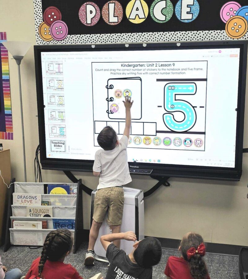 kindergarten student moving images on a teaching slide for the number five. 