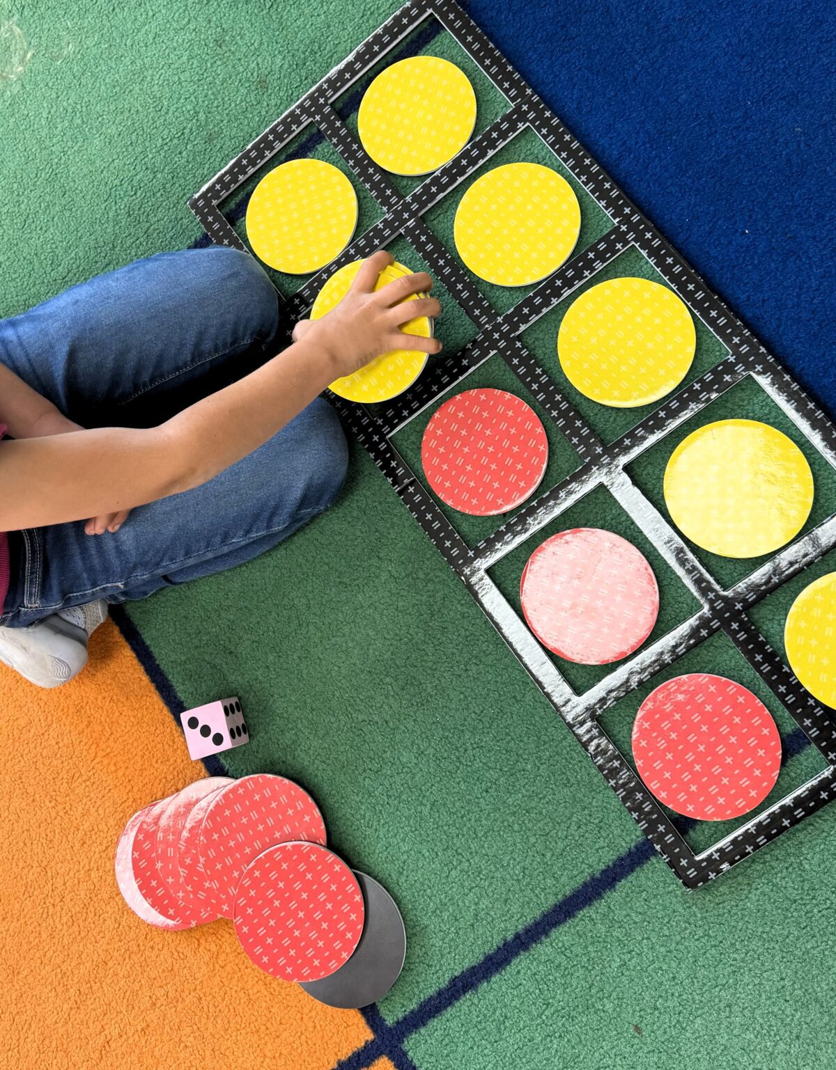 Student moving counters in a large ten frame on the rug to add and subtract in first grade. 