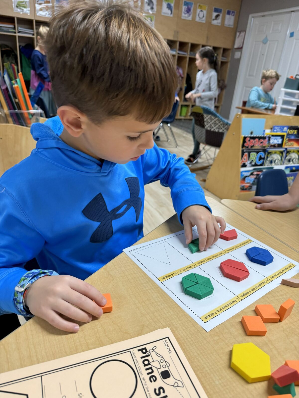 Student using pattern blocks to sort and build 2D shapes during a hands-on elementary math activity.